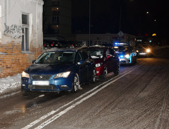 na ulicy stoją dwa samochody osobowe, za nimi policyjny radiowóz