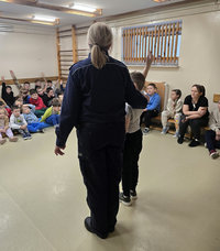 policjantka z dzieckiem oraz siedzące wokół dzieci w czasie spotkania profilaktycznego