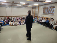 odwrócona tyłem policjantka stoi przed siedzącymi na podłodze dziećmi w czasie spotkania profilaktycznego