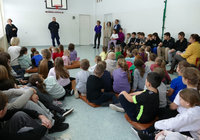 policjant stoi przed siedzącymi na podłodze dziećmi w czasie spotkania profilaktycznego