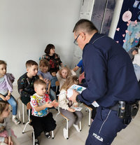 policjant w czasie spotkania profilaktycznego rozdaje przedszkolakom kolorowanki