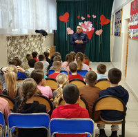 policjant stoi przed siedzącymi na krzesłach dziećmi w czasie spotkania profilaktycznego