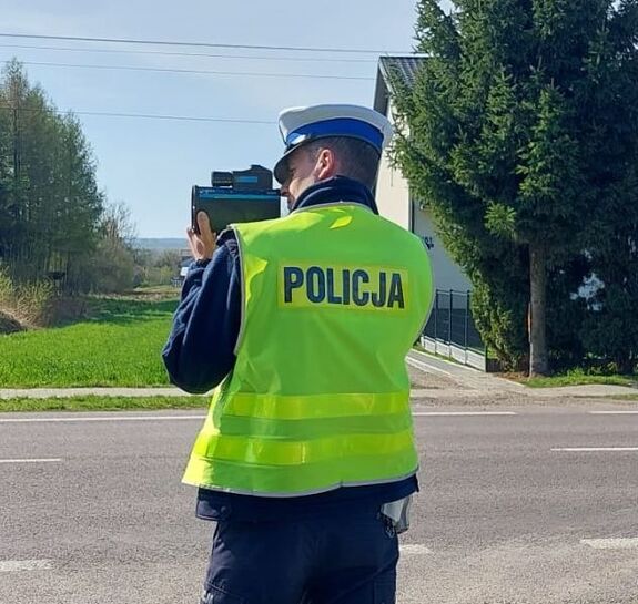 policjant stoi na poboczu drogi i urządzeniem mierzy prędkość jazdy kierujących