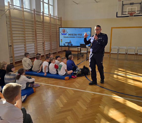 policjant rozmawia z uczniami w czasie spotkania profilaktycznego w ramach akcji Misja 112