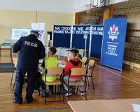policjant stoi obok uczniów siedzących w ławce