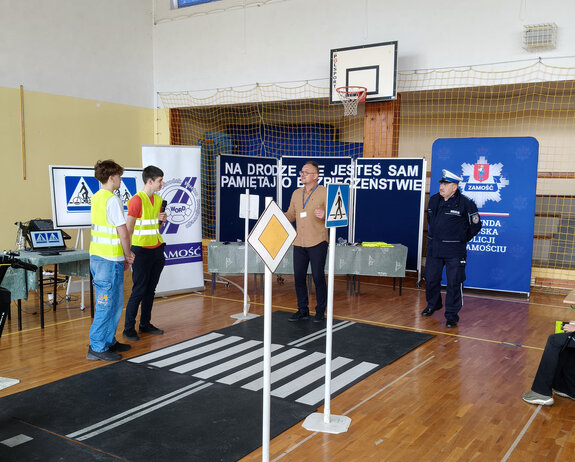 policjant i pracownik Wojewódzkiego Ośrodka Ruchu Drogowego obok dwóch chłopców na makiecie miasteczka ruchu drogowego