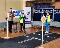 pracownik Wojewódzkiego Ośrodka Ruchu Drogowego obok dwóch chłopców na makiecie miasteczka ruchu drogowego, jeden z chłopców trzyma hulajnogę