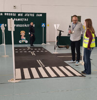 pracownik Wojewódzkiego Ośrodka Ruchu Drogowego i uczennica obok hulajnogi, w tle policjant