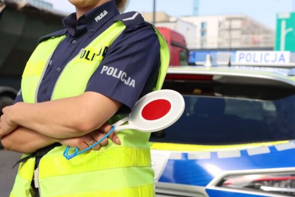 policjantka z tarczą do zatrzymywania pojazdów, w tle radiowóz