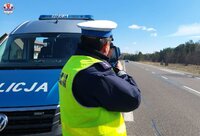 policjant z miernikiem prędkości stoi obok radiowozu