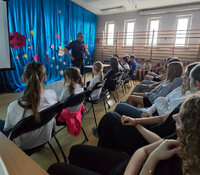 policjant stoi przed siedzącymi na krzesłach uczniami w czasie spotkania profilaktycznego