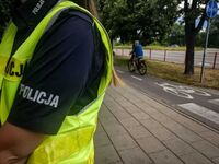 stojąca bokiem policjantka a za nią ścieżka rowerowa po której jedzie rowerzysta