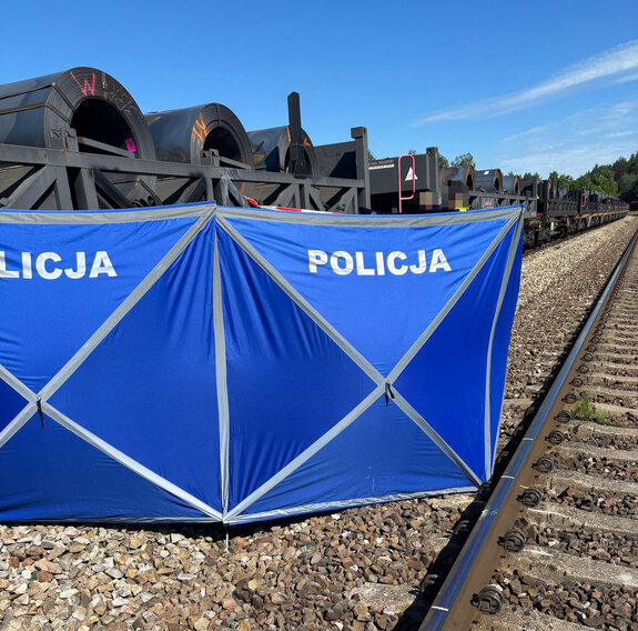 policyjny parawan obok torów na których stoi pociąg towarowy