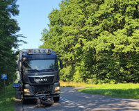 Na drodze leży przewrócony motocykl, którego kierujący uderzył w ciężarówkę. Ciężarówka stoi na drodze za motocyklem.