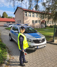 policjantka przed radiowozem zaparkowanym we wjeździe na teren szkoły