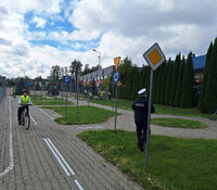 policjant na miasteczku rowerowym obserwuje jak rowerem poruszają się młodzi cykliści