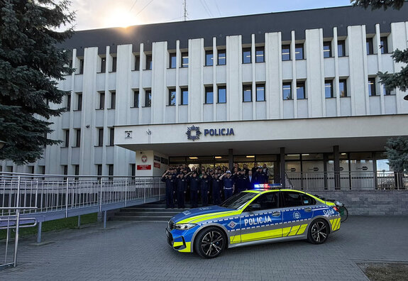 policjanci przed budynkiem Komendy Miejskiej Policji w Zamościu, przed nimi radiowóz
