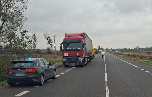 nieoznakowany radiowóz, policjant na drodze i kolejka tirów