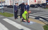 policjant i trzej mężczyźni przy przejściu dla pieszych. Jeden z mężczyzn maluje farbą chodnik przed przejściem dla pieszych